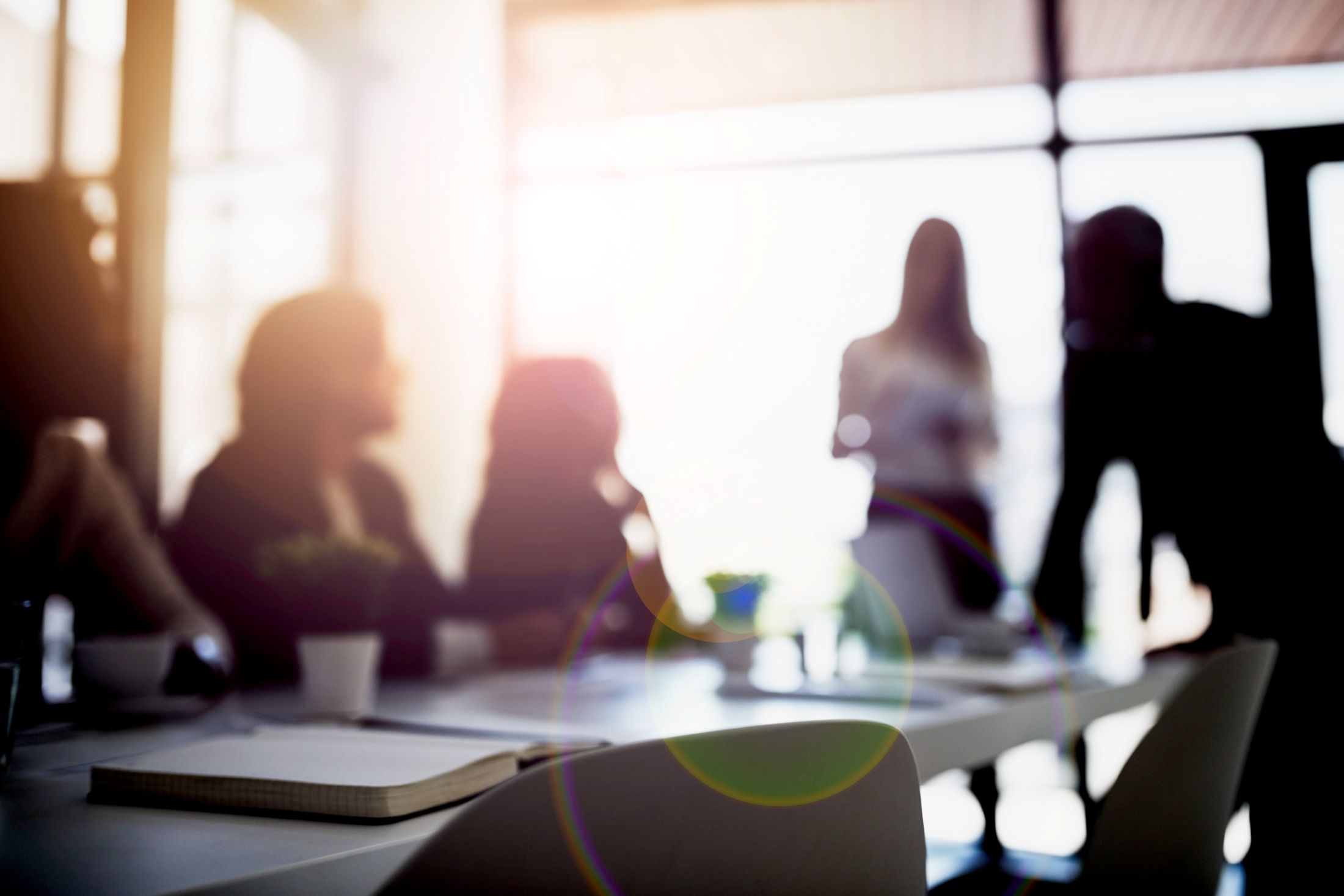 A blurred background image of a team at work around a conference table, illustrating an RIA financial team consulting about the best way to go independent.